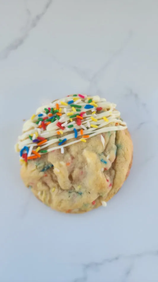 Funfetti cookie topped with white icing and colorful sprinkles