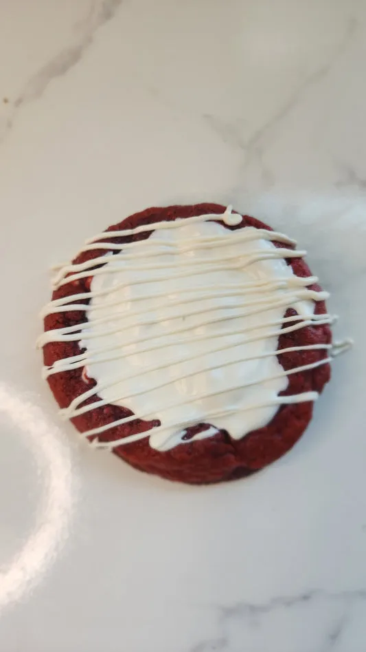 Red velvet cookie topped with cream cheese icing and white drizzle